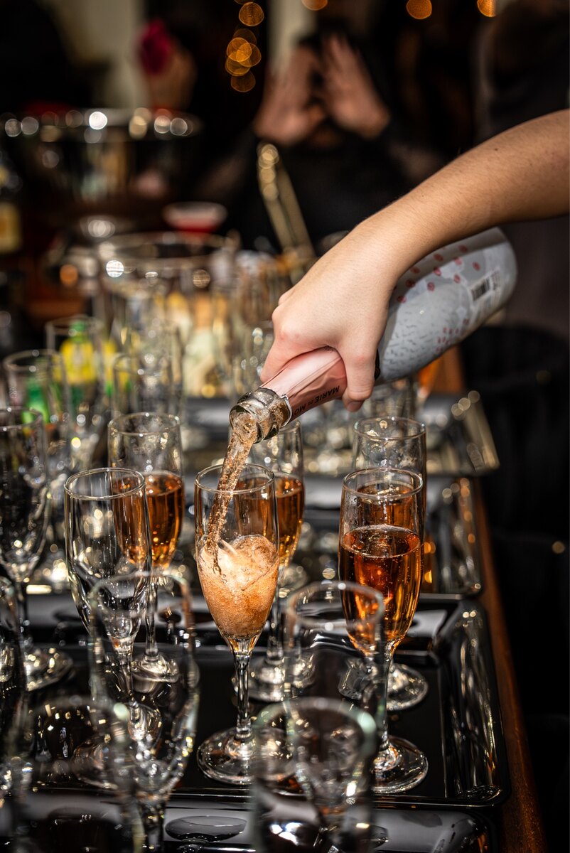 A bartender pouring a finished cocktail into a row of glasses during event service.