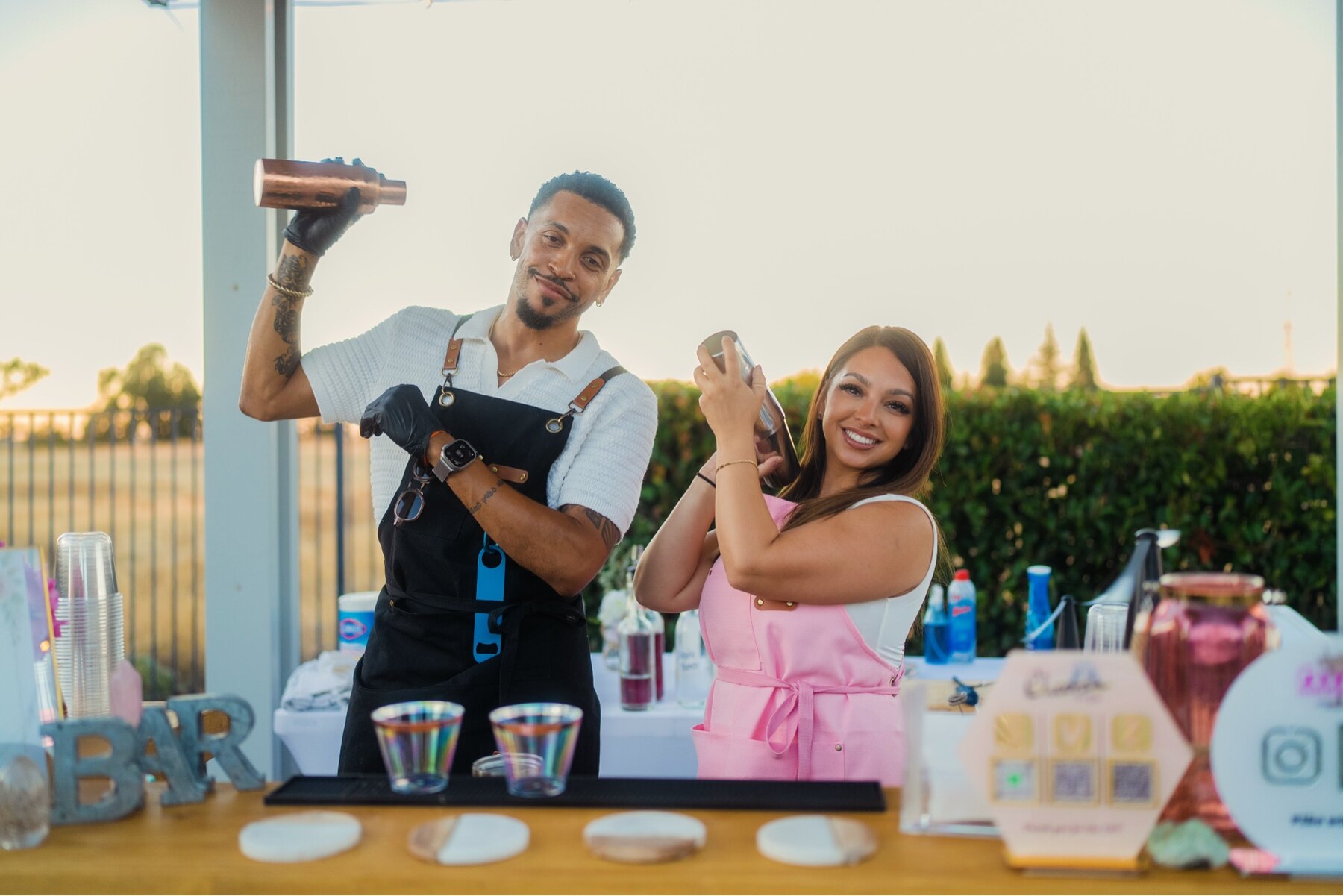 Owners Tyler and Jacque smiling and serving drinks together behind their mobile bar.