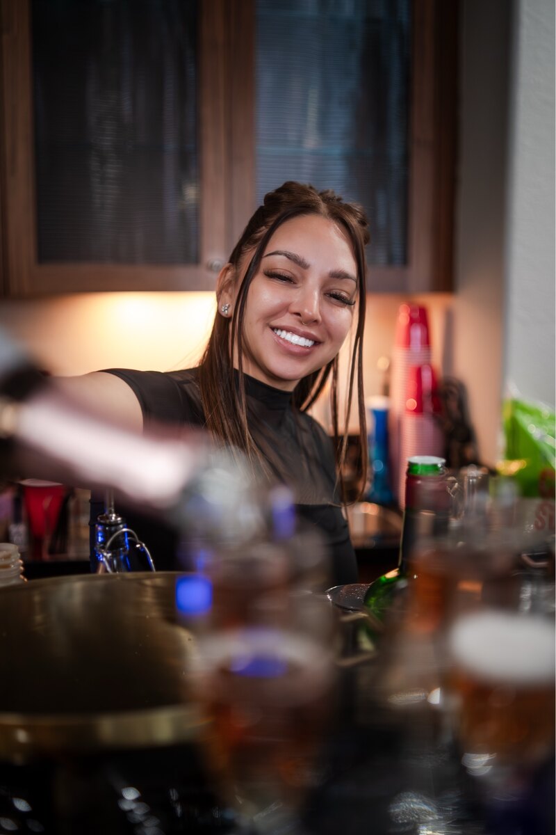 Jacque smiling while preparing a drink behind the bar at a 916 Pour Decisions event.